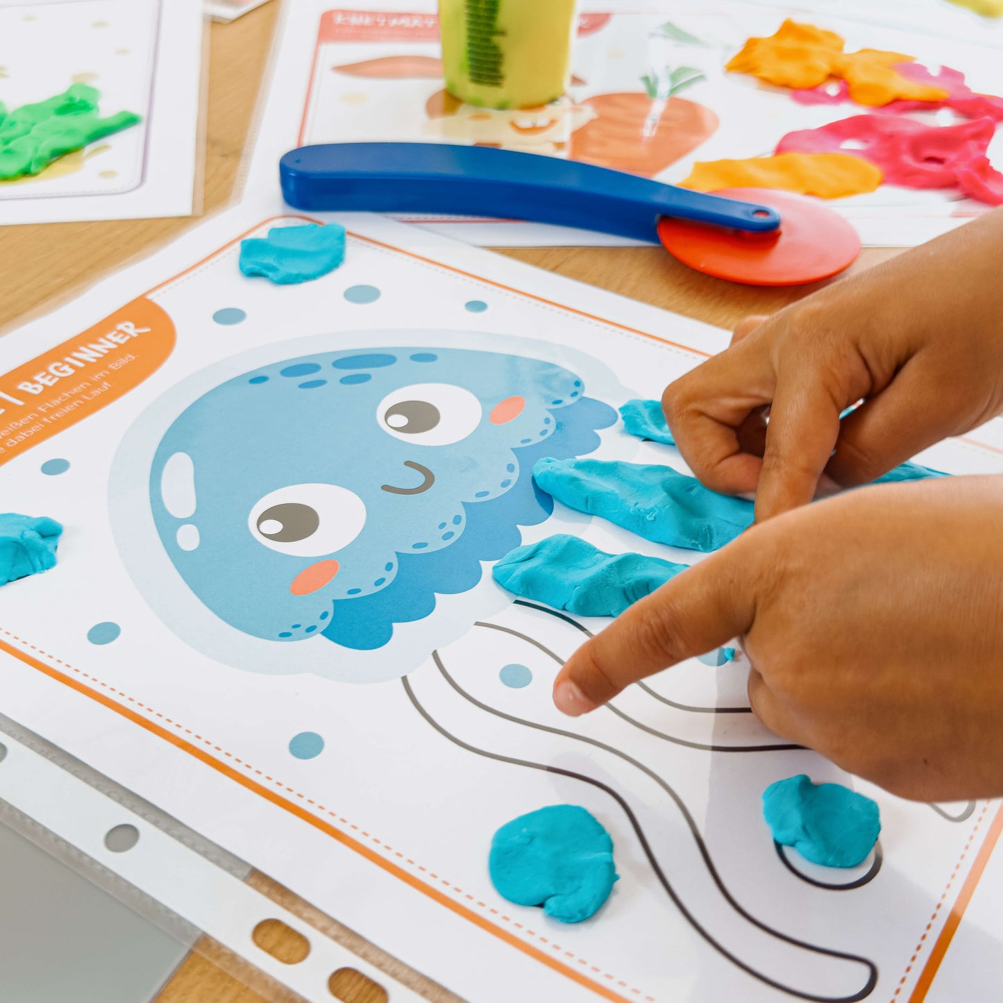 Auf einer mykidslounge Beginner Knetmatte formt ein Kind mit türkisfarbener Knete die Tentakel einer freundlichen Qualle – spielerisches Fördern der Feinmotorik.