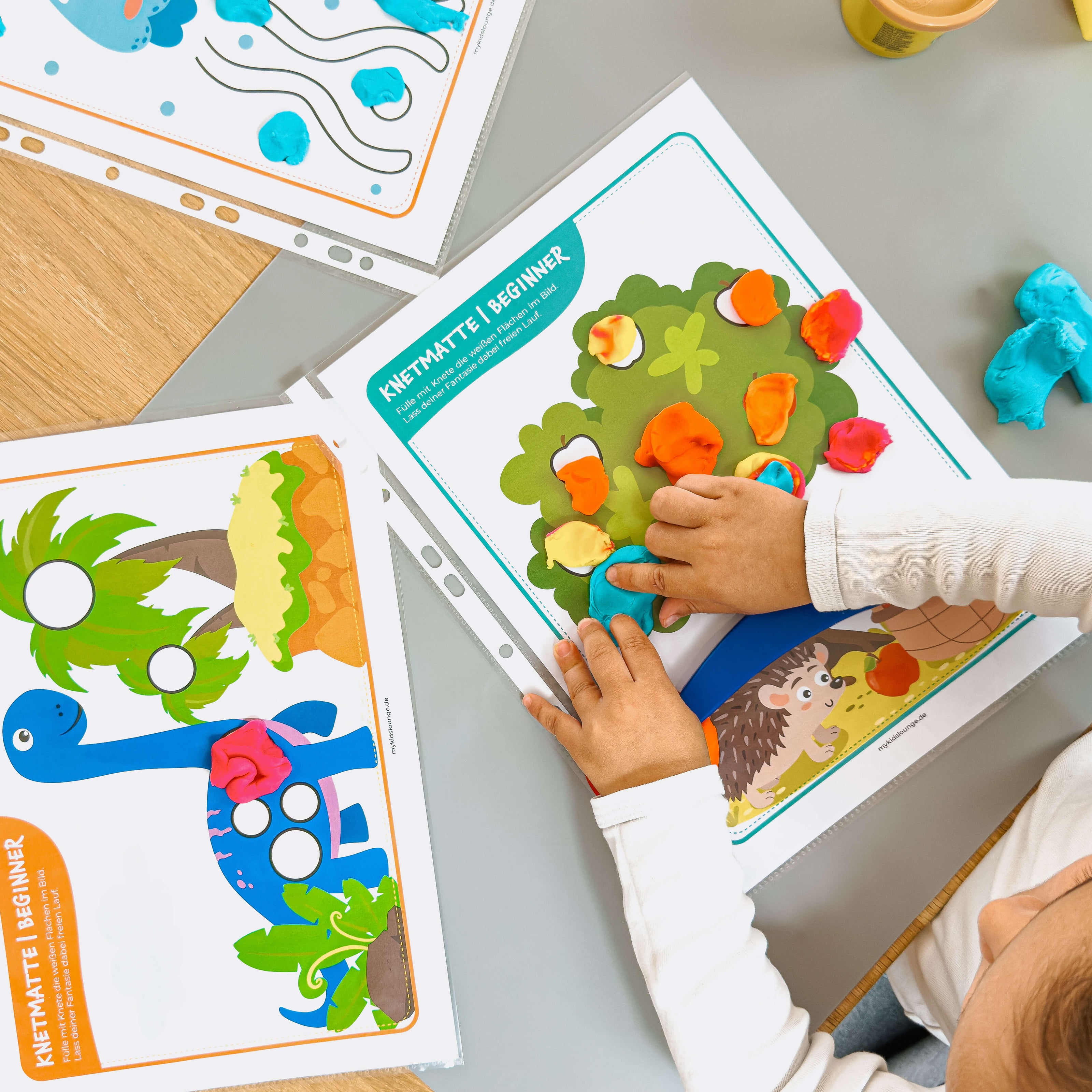 Auf einer mykidslounge Beginner Knetmatte formt ein Kind mit Knete bunte Äpfel für einen Baum – ideales Training für die Feinmotorik und Farbenlernen.