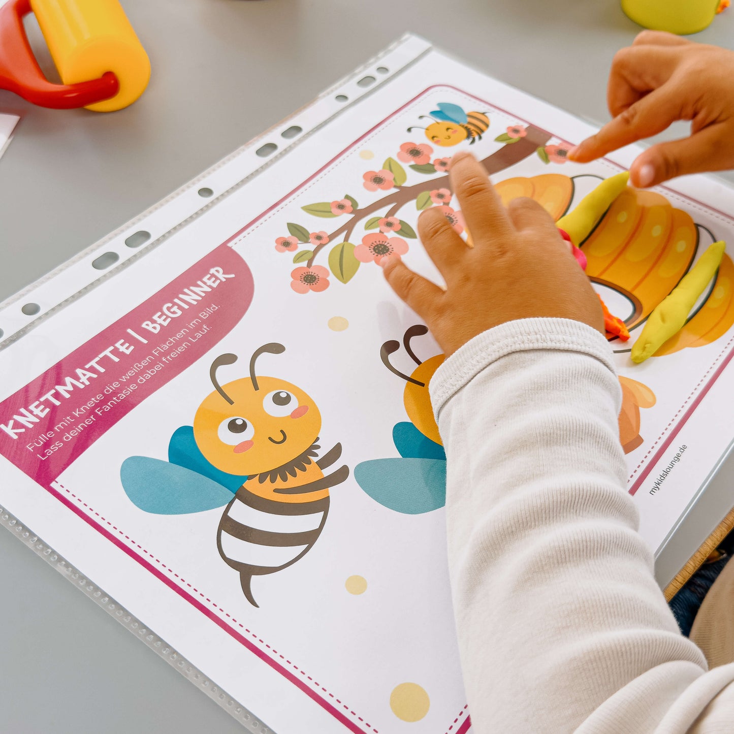 Kind drückt bunte Knete auf Blüten und Bienenstock einer liebevoll gestalteten mykidslounge Beginner Knetmatte – perfekt für kreatives Gestalten mit kleinen Händen.
