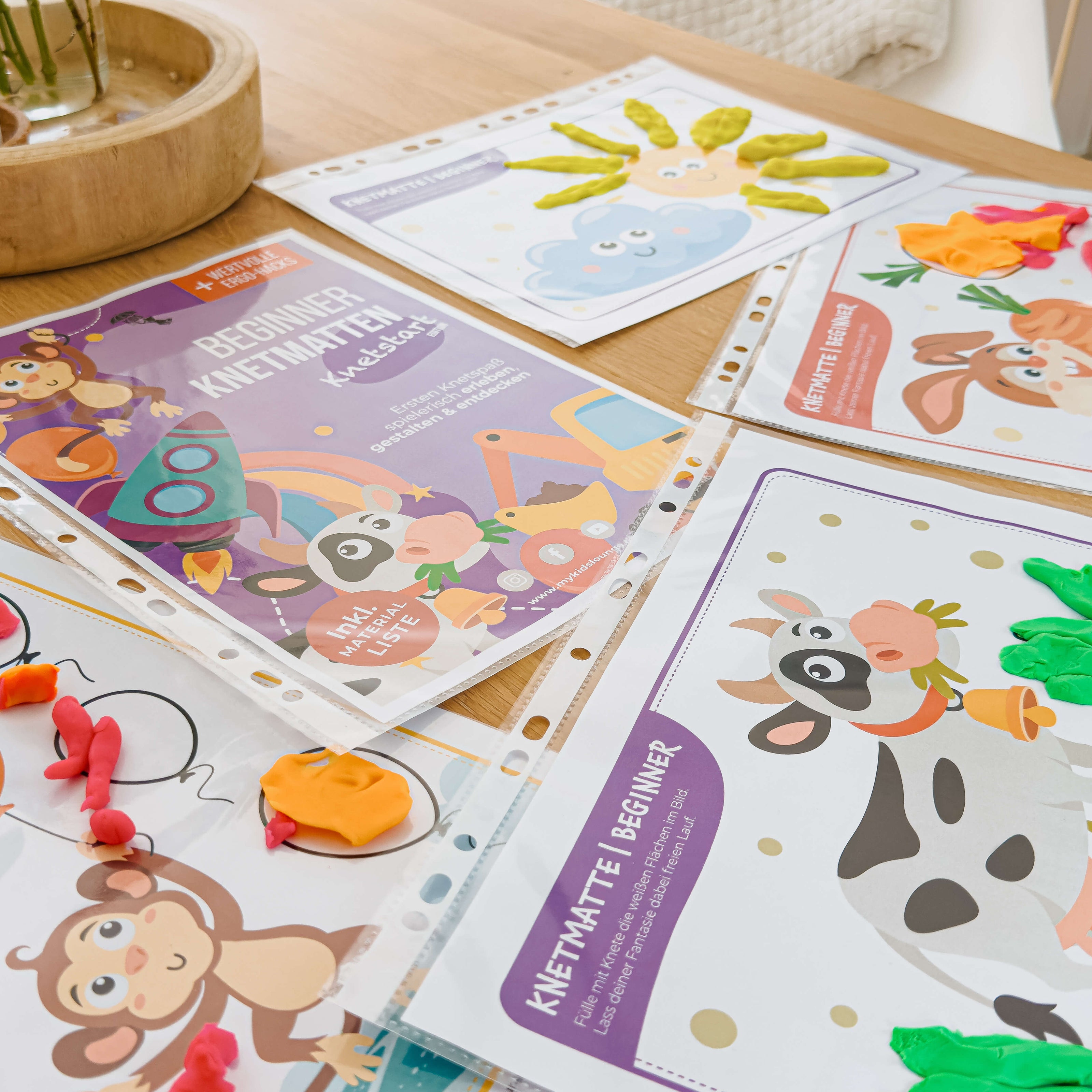 Mehrere liebevoll gestaltete Beginner Knetmatten von mykidslounge auf einem Tisch ausgelegt, inklusive Cover und Motiven wie Kuh, Affe, Rakete und Sonne – perfekt für den Knetstart.