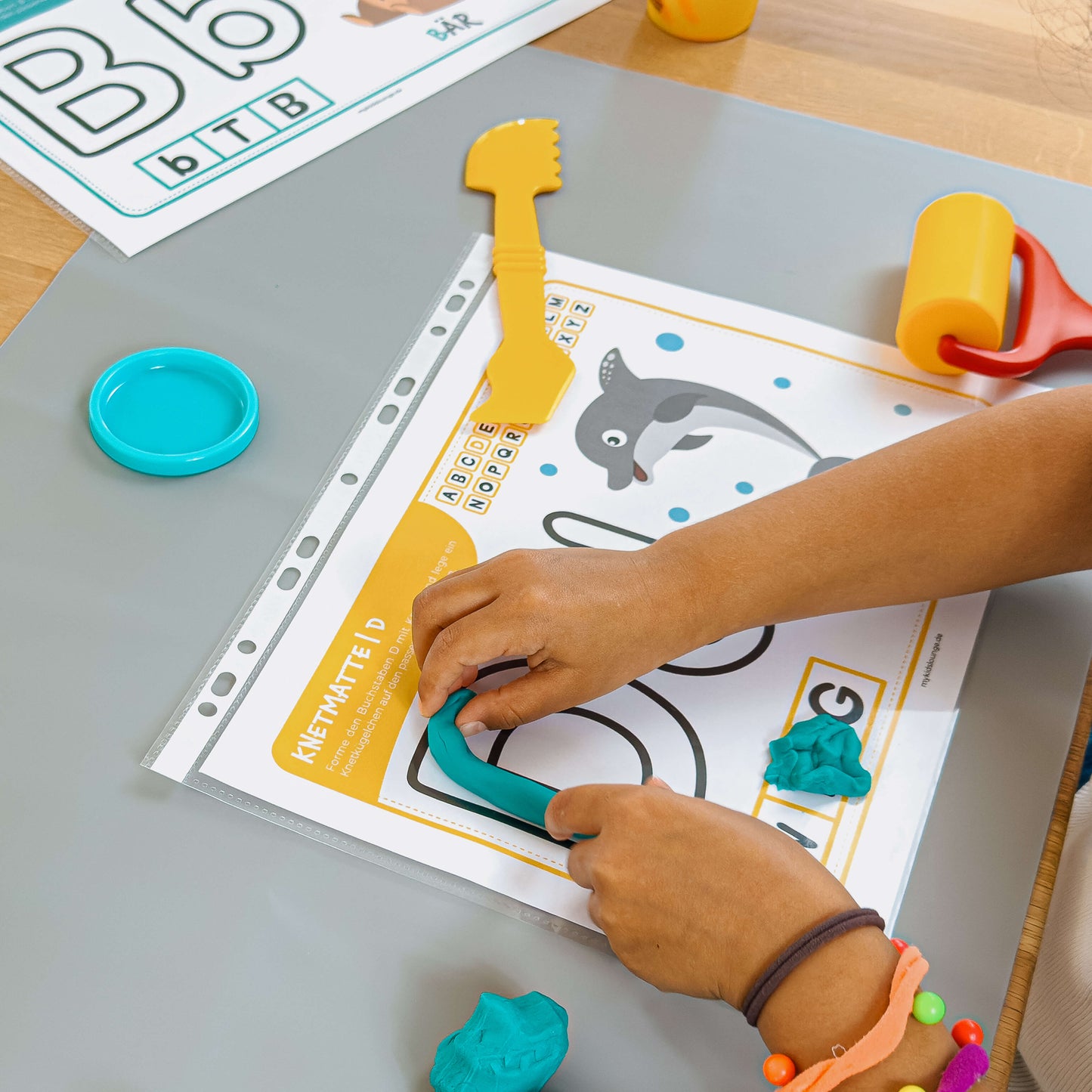 Kind formt mit blauer Knete den Buchstaben D auf der mykidslounge Knetmatte – spielerisches Buchstabenlernen mit Delfin-Motiv.