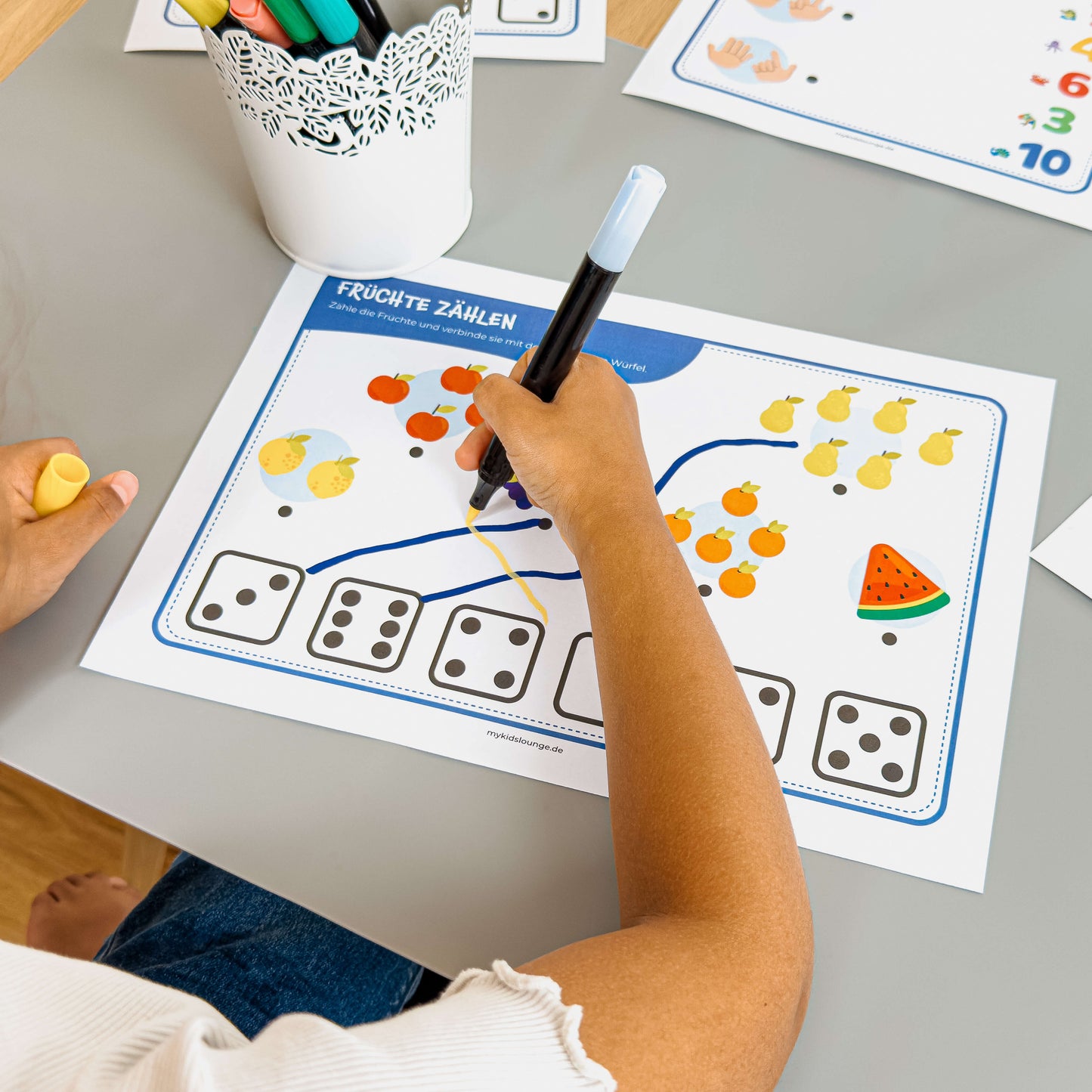 mykidslounge Zählübung Früchte & Würfel. Kind verbindet Zahlen mit Früchten – spielerische Förderung von Mengenverständnis und Auge-Hand-Koordination.