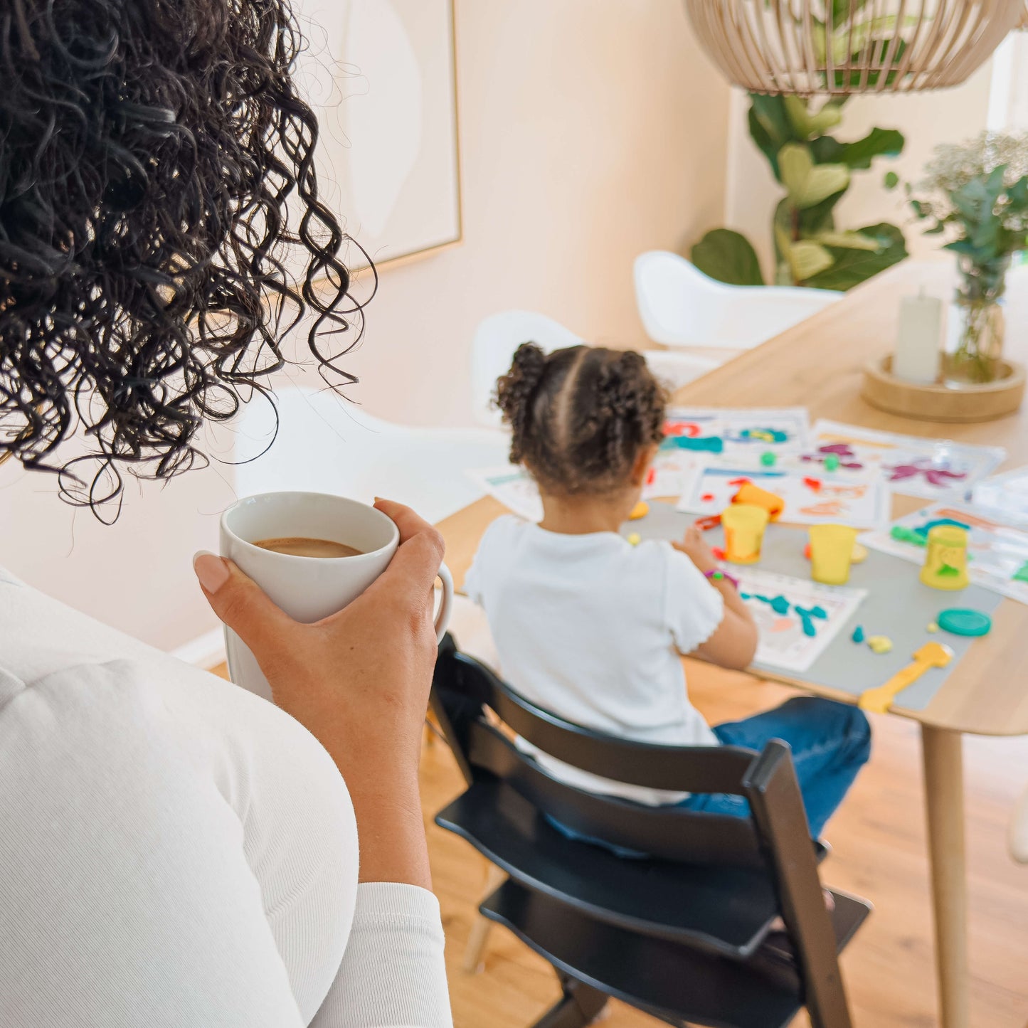 Mama genießt ihre Auszeit mit Kaffee, während ihr Kind selbstständig mit den mykidslounge Knetmatten spielt – entspannte Lernzeit zu Hause.