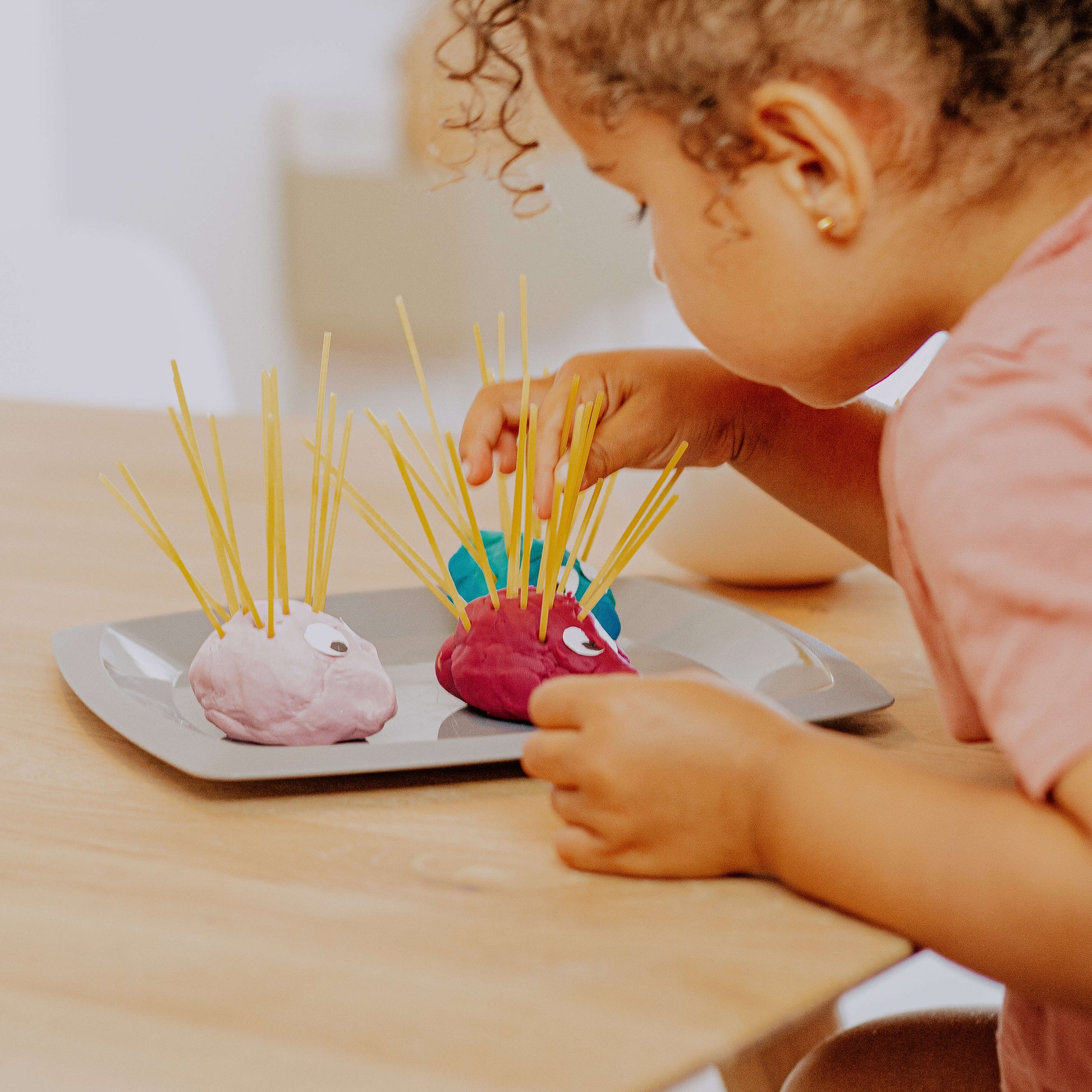 Kleinkind spielt die Spielidee Igelfamilie am Esstisch und steckt Spaghetti in bunte Knete 