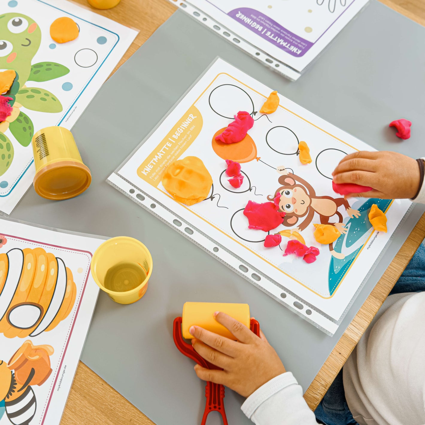 Kind gestaltet mit bunter Knete Luftballons auf einer mykidslounge Beginner Knetmatte mit einem fröhlichen Affen – fördert gezielt die Hand-Auge-Koordination.