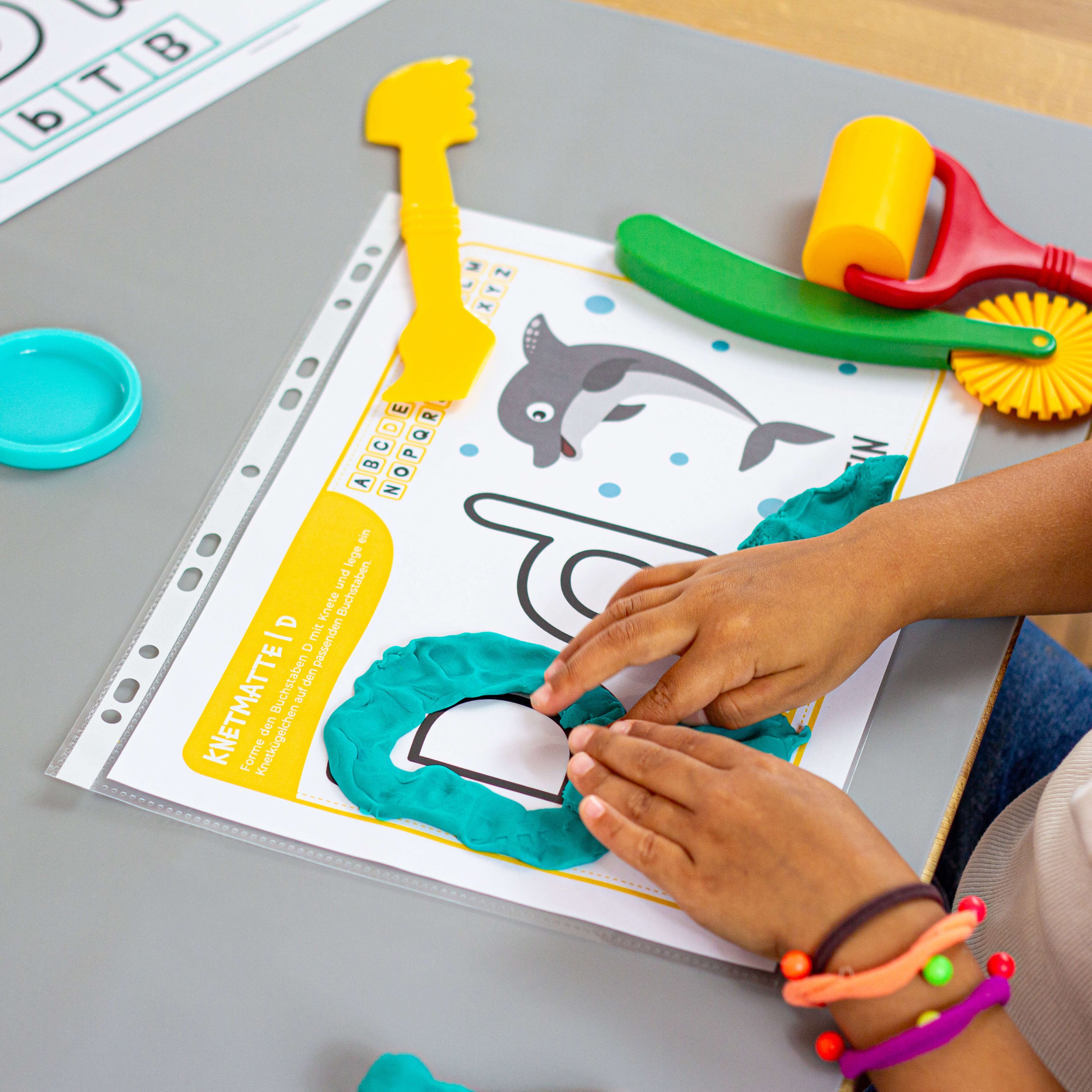 Feinmotorik fördern und Buchstaben begreifen – Kind bedeckt den Buchstaben D mit Knete auf der liebevoll gestalteten Lernmatte.