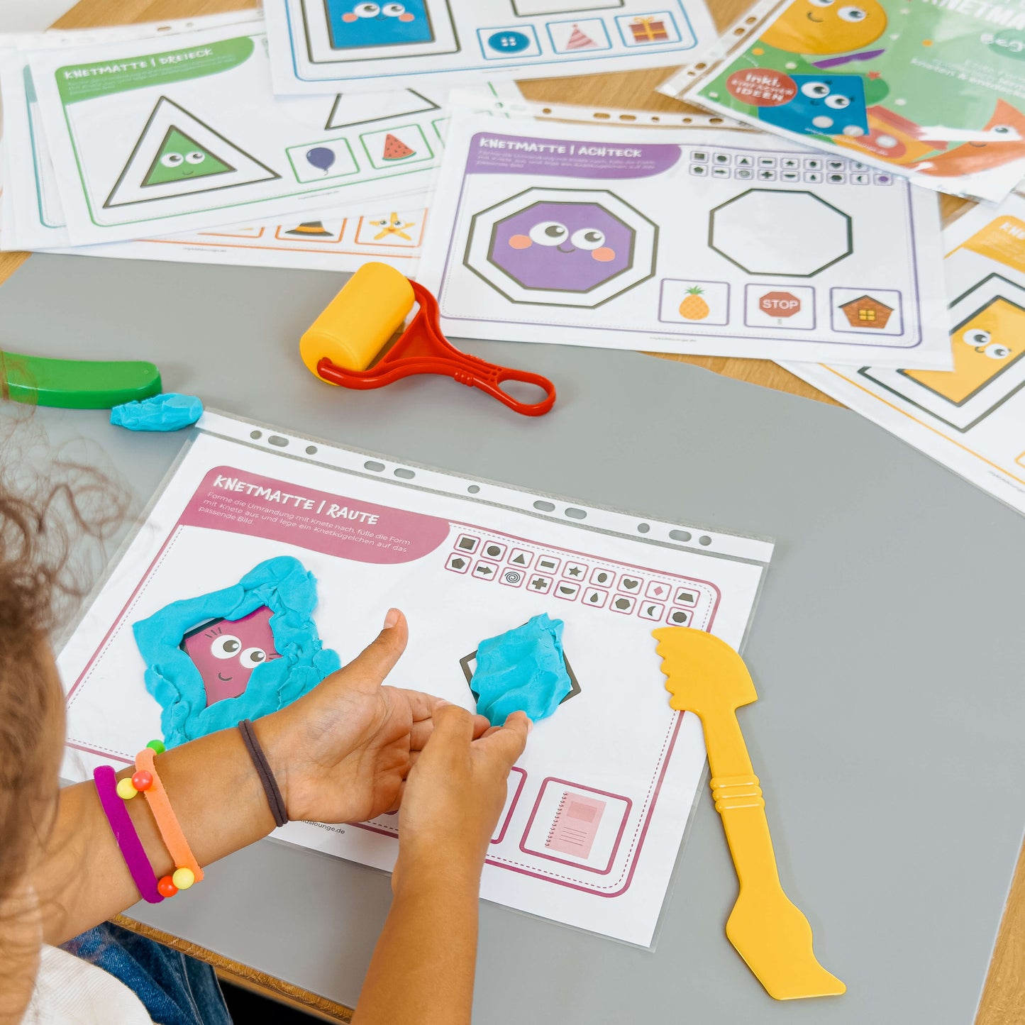 Vielfältige Formen-Knetmatten im Einsatz. Ein Kind modelliert eine Raute mit blauer Knete und entdeckt verschiedene geometrische Formen.